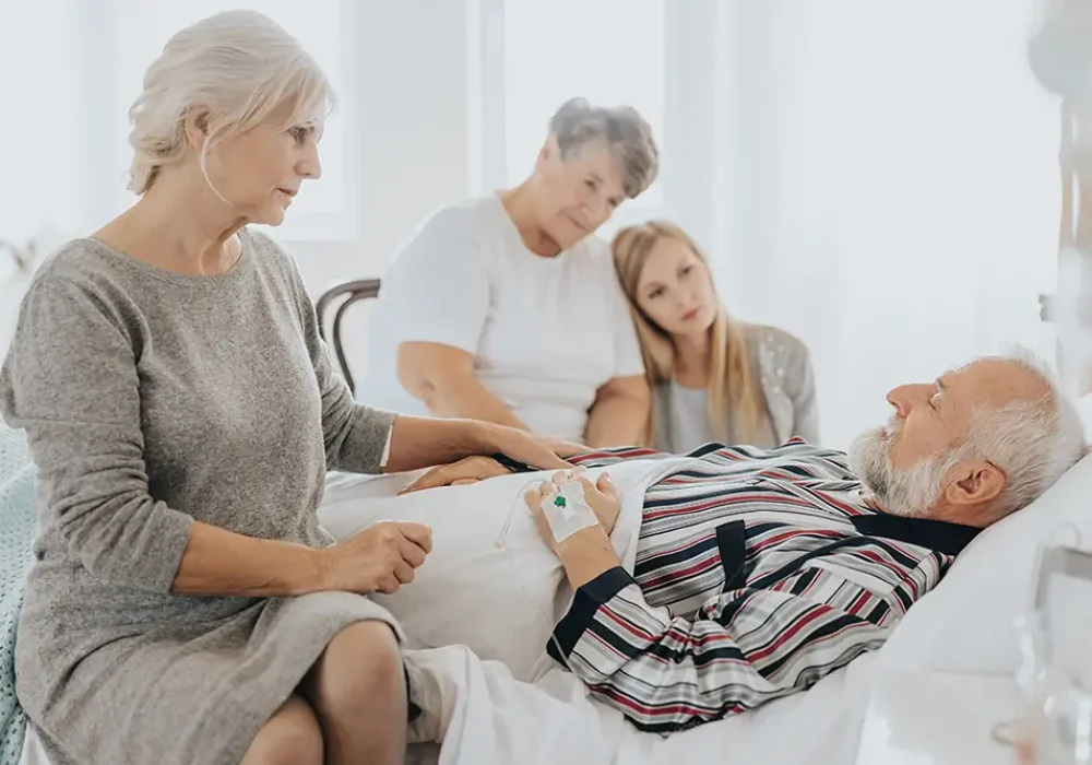 Senior palliative patient lying in hospital bed supported by loving family